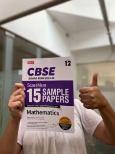 person showing thumbs up with scoremore sample paper class 10 math book